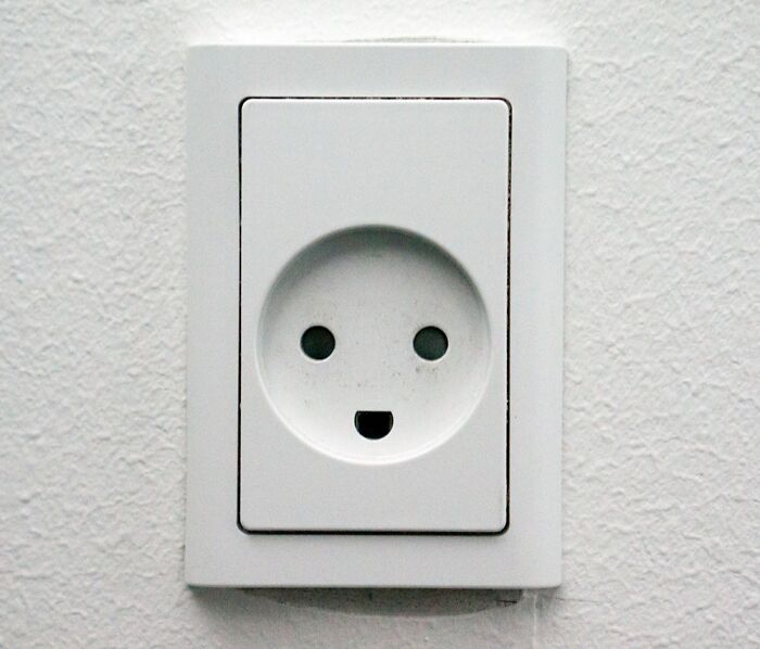 White electrical outlet on a textured wall resembling a face, illustrating unique design in a Danish prison cell.