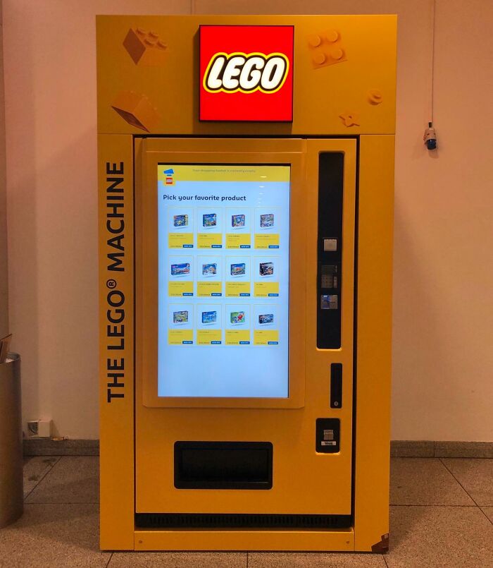 Yellow LEGO vending machine with touchscreen display showing product options inside a Danish prison cell setting.