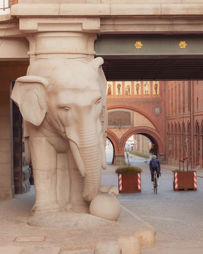 Stone elephant sculpture under a bridge in Denmark with a cyclist riding nearby, showcasing Danish architecture and street art.