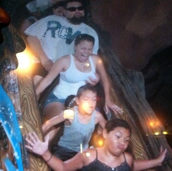 Family of four captured in a candid moment on a log flume ride at an amusement park, showing mixed emotions and excitement.