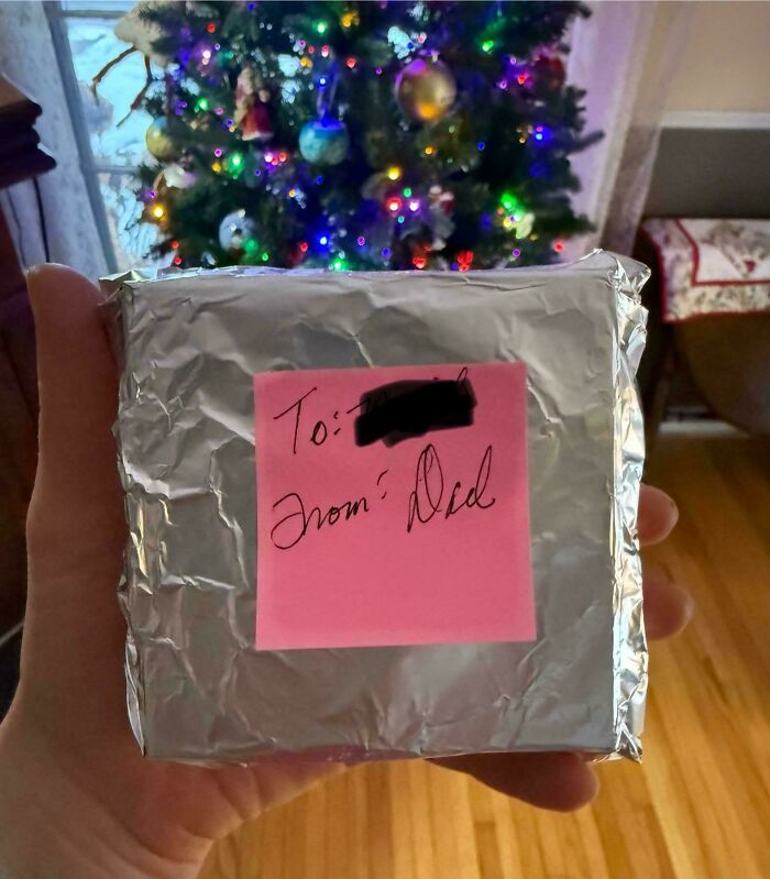 Gift wrapped in aluminum foil with a humorous note from dad, shown in front of a decorated Christmas tree, funny parents moment.