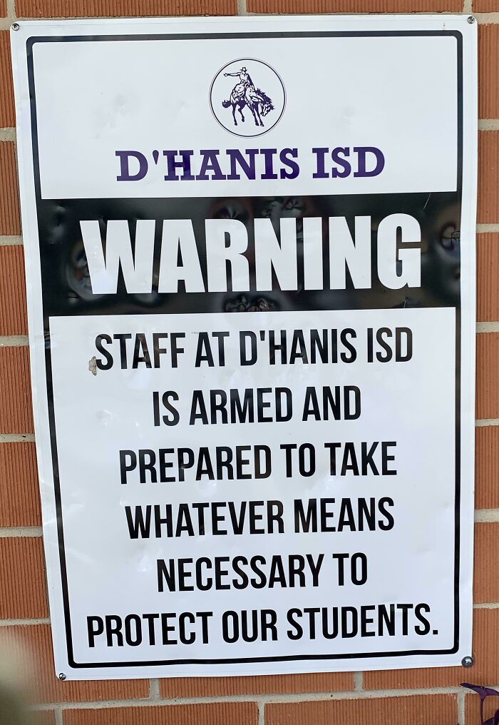 Warning sign at school showing armed staff prepared to protect students in a real-life dystopian US scene.