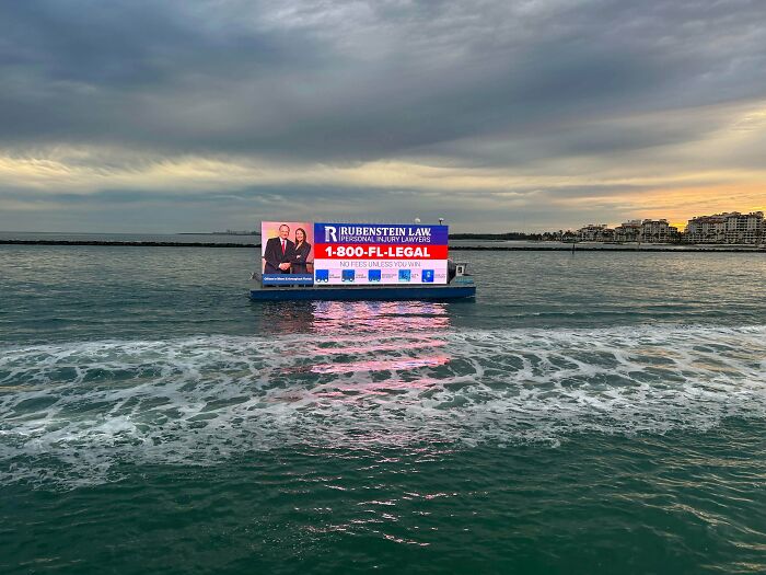 Floating billboard for personal injury lawyers on ocean water under a gloomy sky in a US coastal city scene.