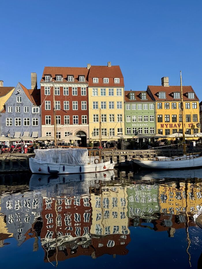 Colorful Danish buildings and boats reflected in calm water along the waterfront, showcasing a vibrant Danish scene.
