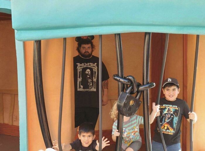 Children posing inside a giant locked cage attraction, a memorable amusement park photo brought home from a trip.