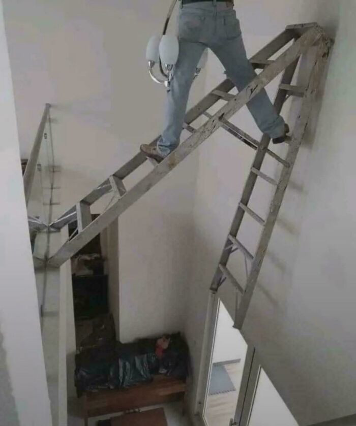Employee ignoring safety protocol by standing on an unstable ladder setup over a high drop inside a building.