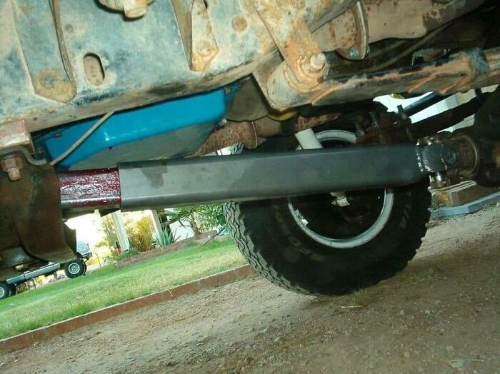 Underside of a vehicle showing a newly installed suspension part and rusted car mechanics components outdoors.