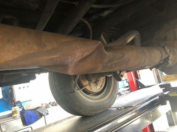 Rusty car exhaust pipe severely dented visible near rear wheel, showing unusual damage car mechanics had to document.