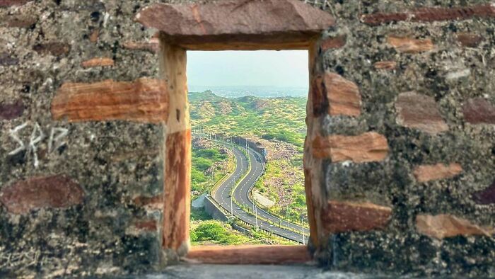 View of a winding road through greenery captured through a stone window in street photography capturing humanity.