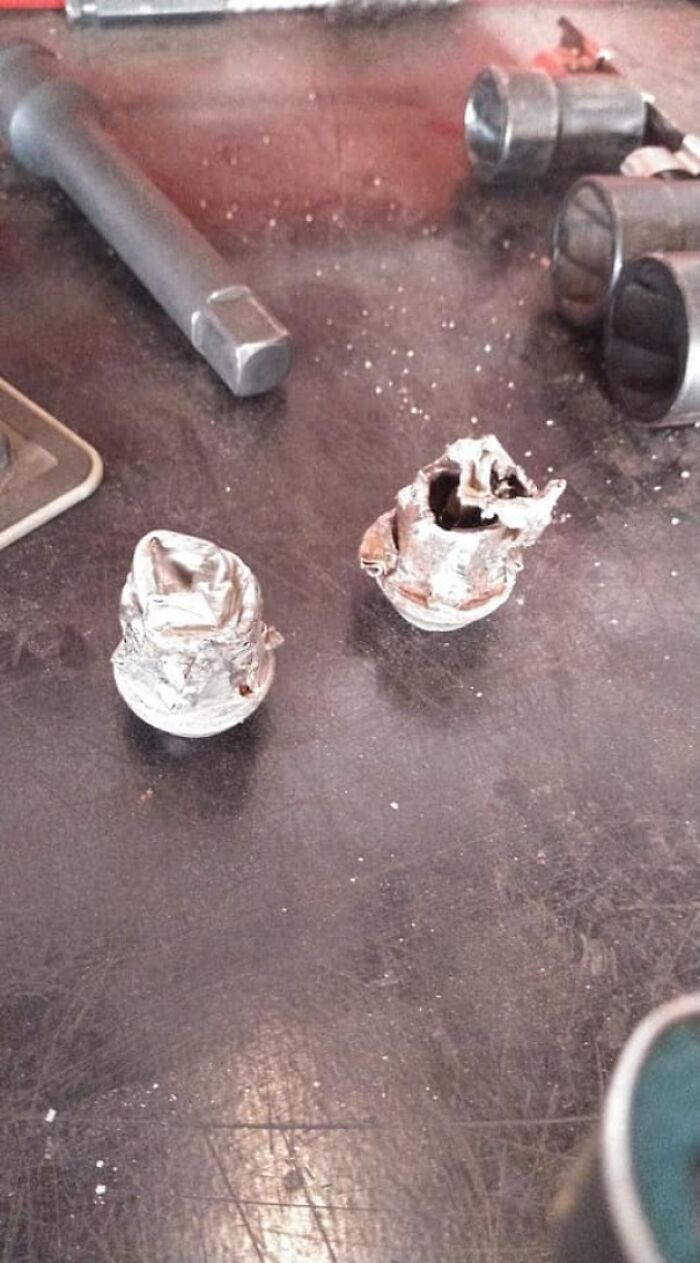 Two damaged and deformed lug nuts on a workshop surface with car mechanic tools in the background.