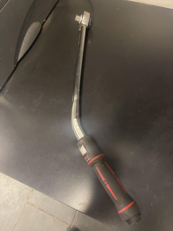 Bent torque wrench with a black and red handle resting on a black surface, showing a mechanic's unusual tool challenge.