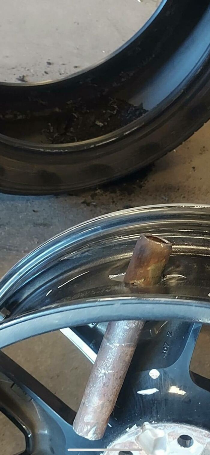 Car mechanic showing rusty metal pipe lodged in a damaged car wheel rim as proof of unusual repair challenges.