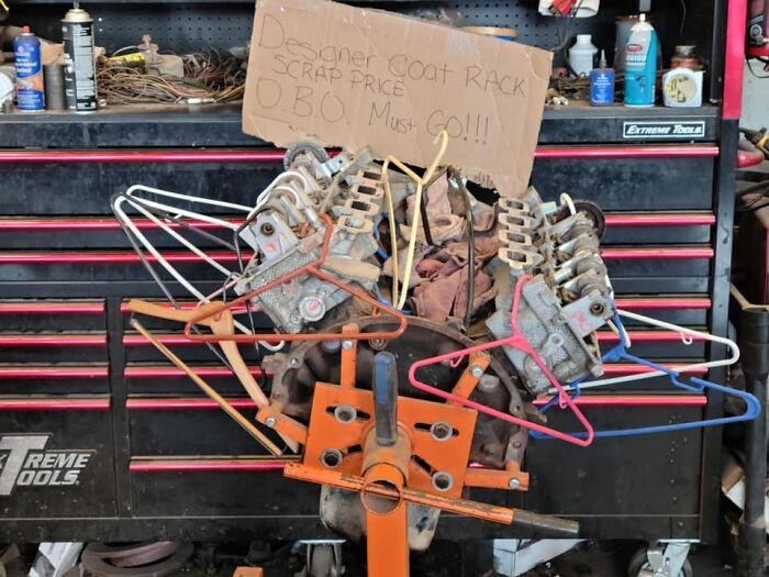 Car mechanics’ unusual engine repair setup with clothes hangers and a handwritten scrap price sign shown in a workshop.