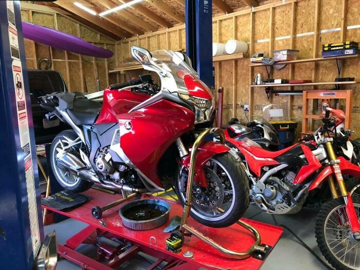 Red motorcycles being serviced in a mechanic’s garage on a hydraulic lift with tools and equipment nearby.