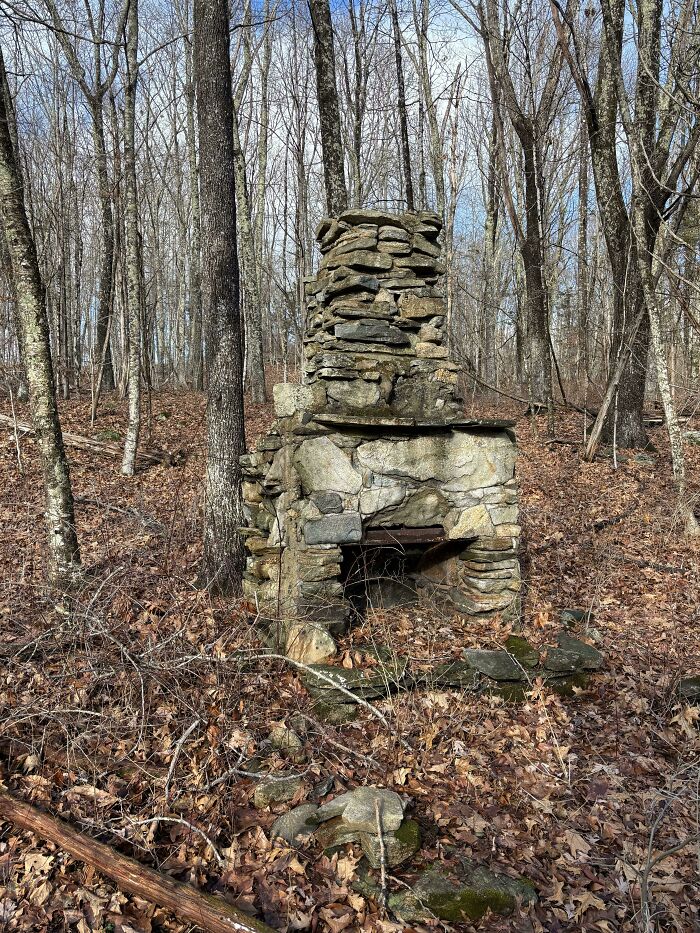 Old stone fireplace standing alone in a forest surrounded by fallen leaves, a curious thing people discovered outdoors. Old stone fireplace standing alone in a forest surrounded by fallen leaves, a curious thing people discovered outdoors.