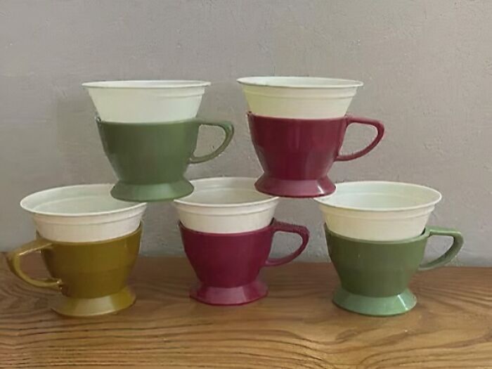 Stacked vintage coffee cups in green, yellow, and maroon colors on a wooden surface, evoking nostalgia and old age.