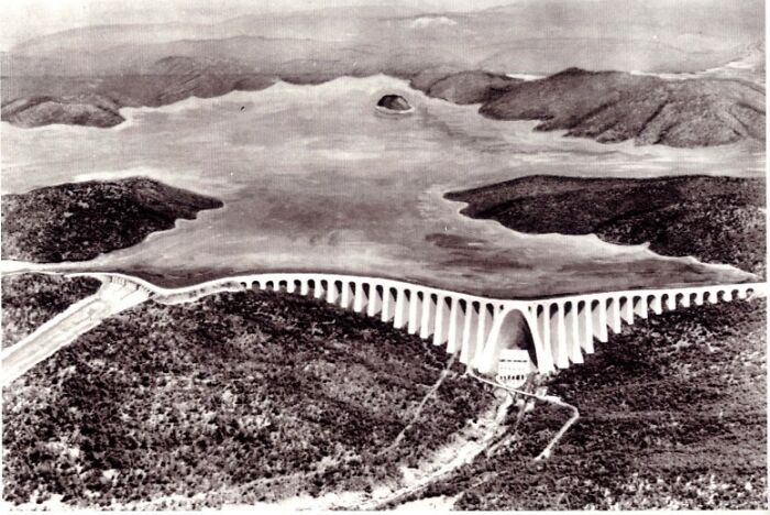 Vintage black and white photo showing a large arched bridge over a river, illustrating peoples lives from a different time.