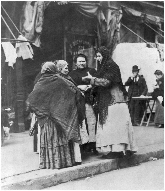 Group of women in old clothing talking on a street, capturing people’s lives from a different time in a vintage photograph.
