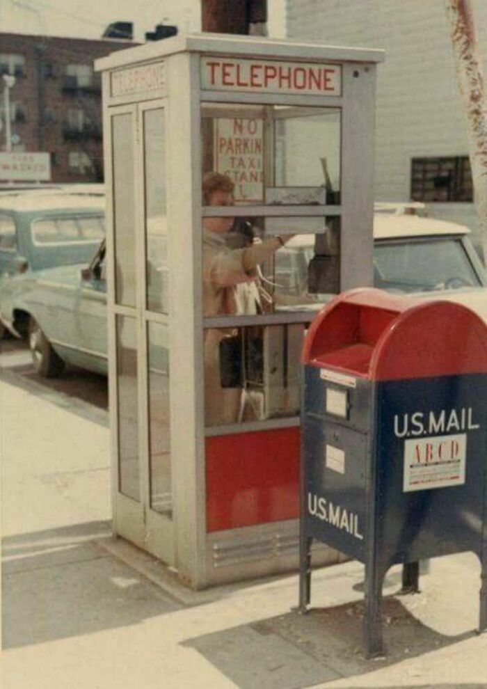 Vintage photo showing a person using a telephone booth next to a U.S. Mail mailbox, capturing lives from a different time.