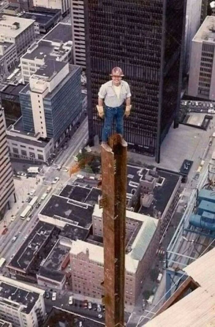 Construction worker standing on steel beam high above city streets in old photo showing people’s lives from a different time