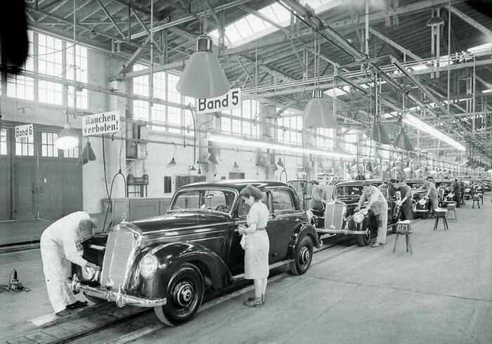 Black and white photo of people assembling classic cars in a factory, showcasing old photos of lives from a different time.