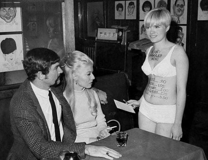 Black and white photo showing people’s lives from a different time with a woman serving customers in vintage attire.