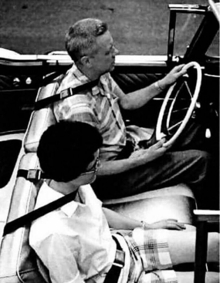 Black and white vintage photo showing two people wearing seat belts inside an old car, reflecting lives from a different time.