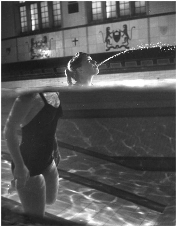Black and white old photo of a woman in a swimming pool spouting water, showcasing lives from a different time.