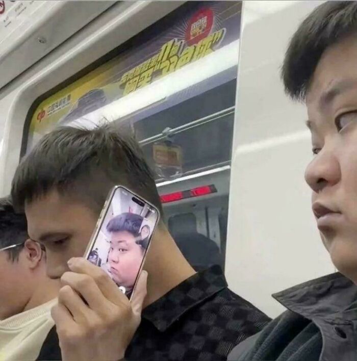 Man on subway holding phone showing a funny face that aligns with his ear combining bizarre and humorous elements.
