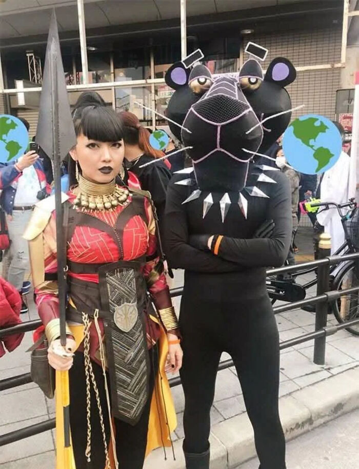 Two people dressed in funny and bizarre costumes, one as a warrior with a spear and the other as a black panther with spikes.
