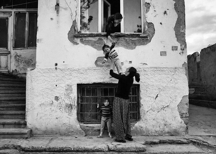 Black and white photo by Yusuf Aksoy showing candid life moments of a woman and children outside an old building in Turkey.