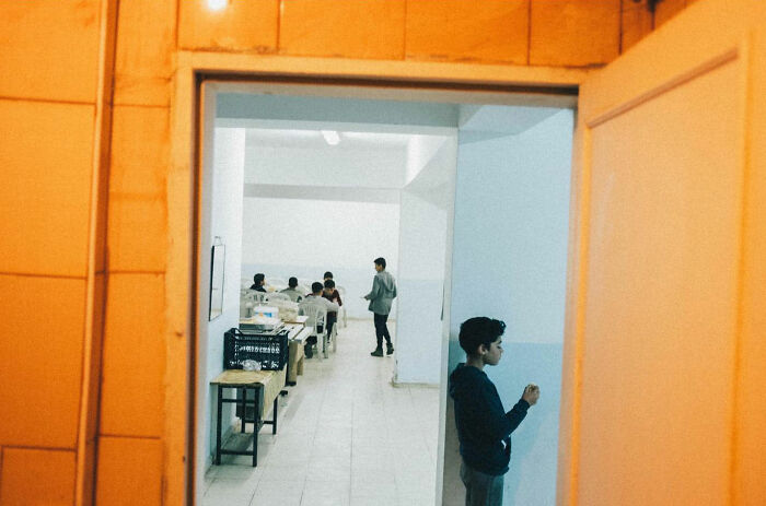 Young boy standing near a doorway with students inside a classroom, showcasing real candid life in Turkey.