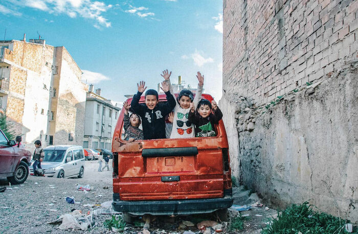 Children joyfully playing in the back of an old red van, showcasing candid life moments in Turkey by Yusuf Aksoy.