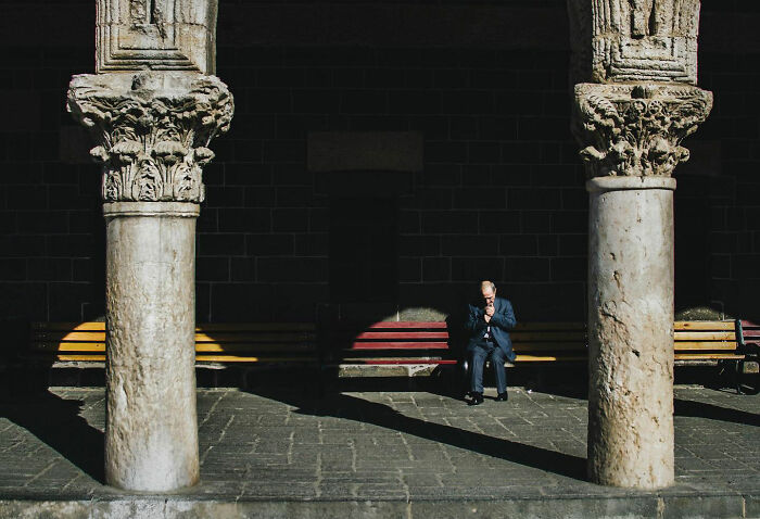 An elderly man sitting on a bench between ancient stone columns, capturing candid life in Turkey.