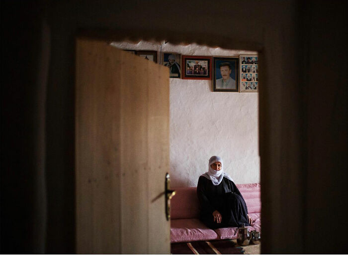 Woman in traditional clothing sitting on a couch inside a home, candid photo capturing real life in Turkey by Yusuf Aksoy.
