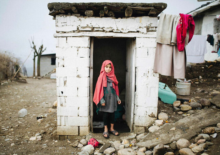 Young girl in traditional clothing standing in the doorway of a simple home, showcasing candid life in Turkey by Yusuf Aksoy.