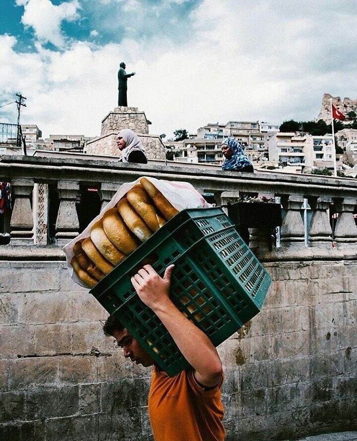 Man carrying bread on his shoulder in a busy street, capturing the real candid side of life in Turkey by Yusuf Aksoy.