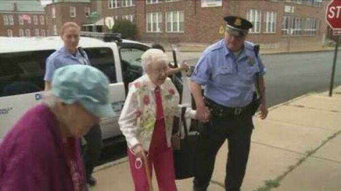 Police officer helping elderly woman walk on sidewalk, a heartwarming story bringing positivity to the world’s negativity.