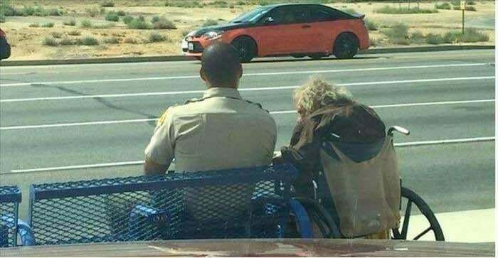 Police officer sitting on a bench next to a person in a wheelchair, a heartwarming moment showing kindness and care.