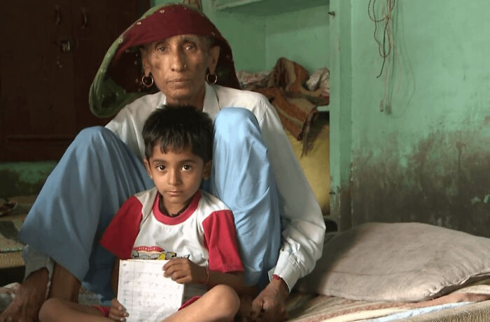 Elderly woman and young boy sitting together in a humble room, sharing a heartwarming moment of connection and care.