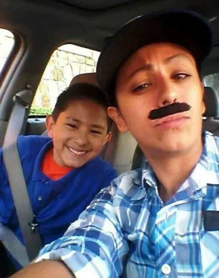 Smiling child and adult with fake mustache inside car, capturing a heartwarming moment for positive stories.