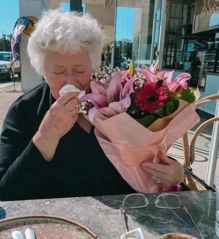 Elderly woman holding a bouquet of flowers, wiping tears, capturing heartwarming stories and positive moments.