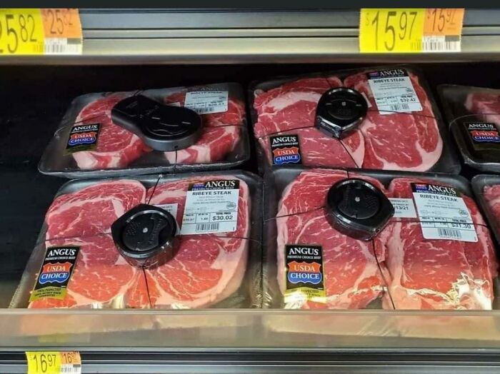 Packages of expensive USDA choice Angus ribeye steak with security tags in a grocery store, highlighting dystopian pricing.
