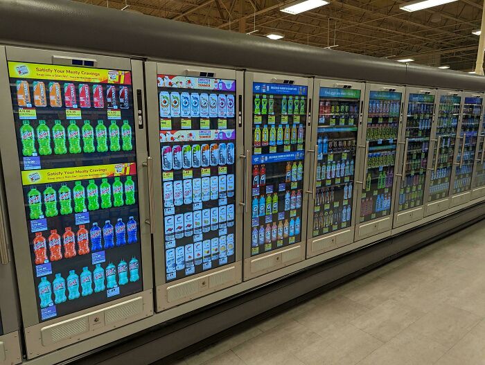 Refrigerated beverage displays with digital screens showing drinks in a modern US supermarket scene.