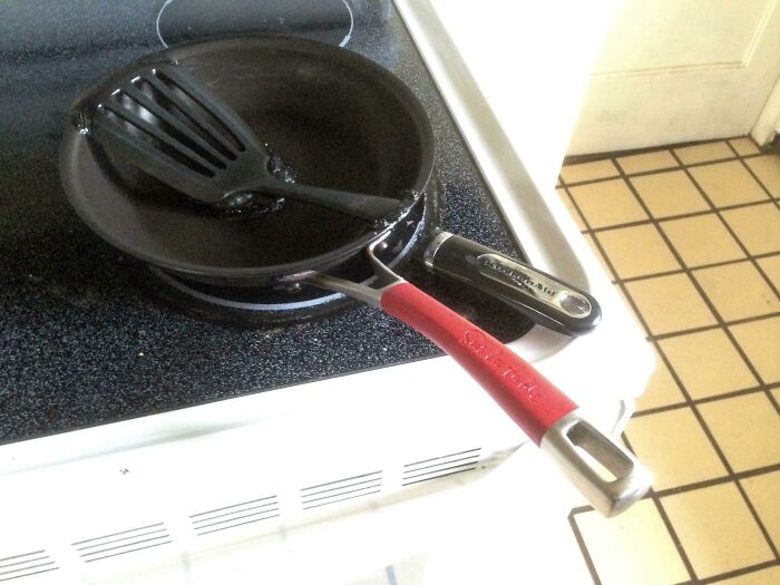 Two frying pans stacked on a stove with a spatula left inside, illustrating awful roommate kitchen habits.