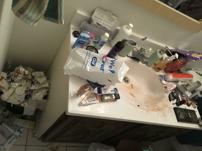 Cluttered bathroom sink with dirty stains and overflowing trash, showing signs of awful roommates and poor hygiene habits.