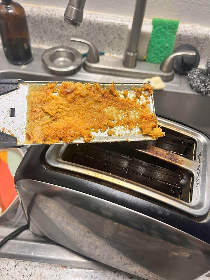 Toaster crumb tray covered in burnt food residue, showing an example of awful roommates neglecting cleanliness.