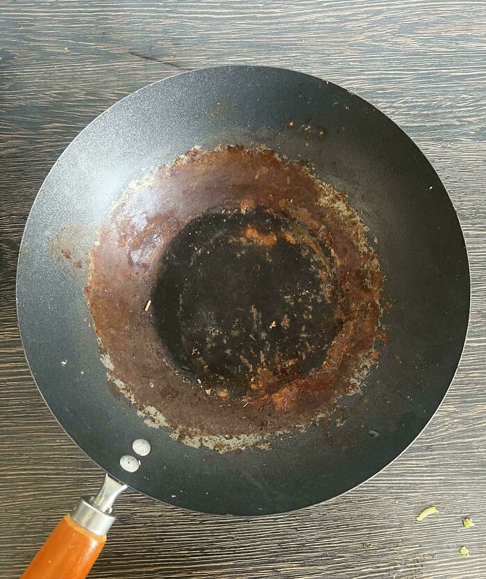 Rusty and dirty frying pan left uncleaned on a wooden surface showing awful roommate neglect.