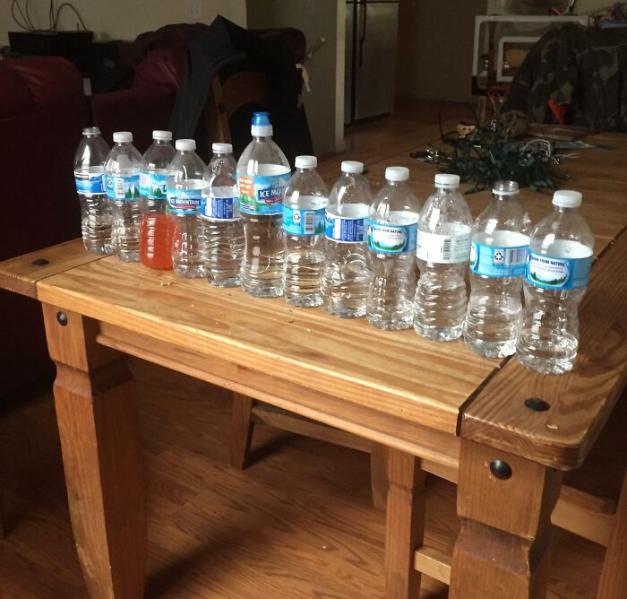 Empty and half-empty water bottles lined up on a wooden table, illustrating annoying habits of awful roommates.