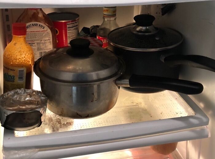 Dirty pots stored inside a fridge surrounded by condiments, showing awful roommate behavior and bad kitchen hygiene.